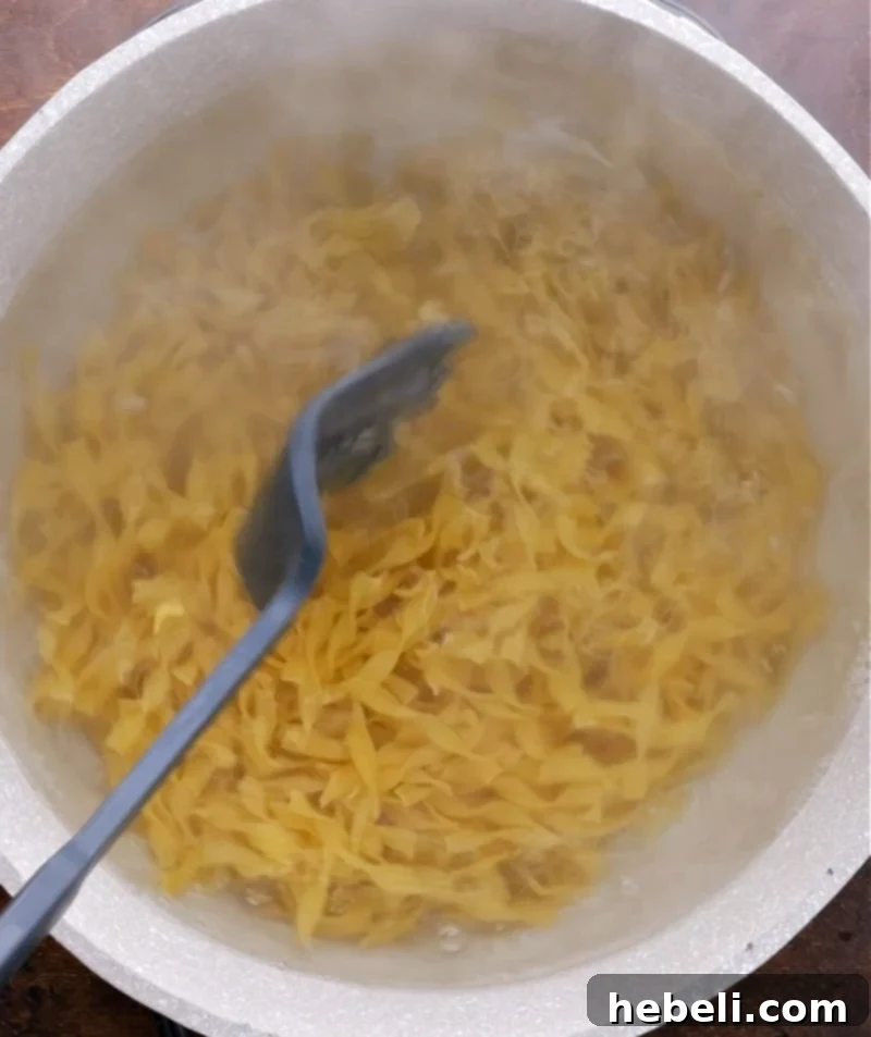 Comforting Ground Beef Supper 5 A pot of egg noodles boiling vigorously on the stove, preparing for the casserole.