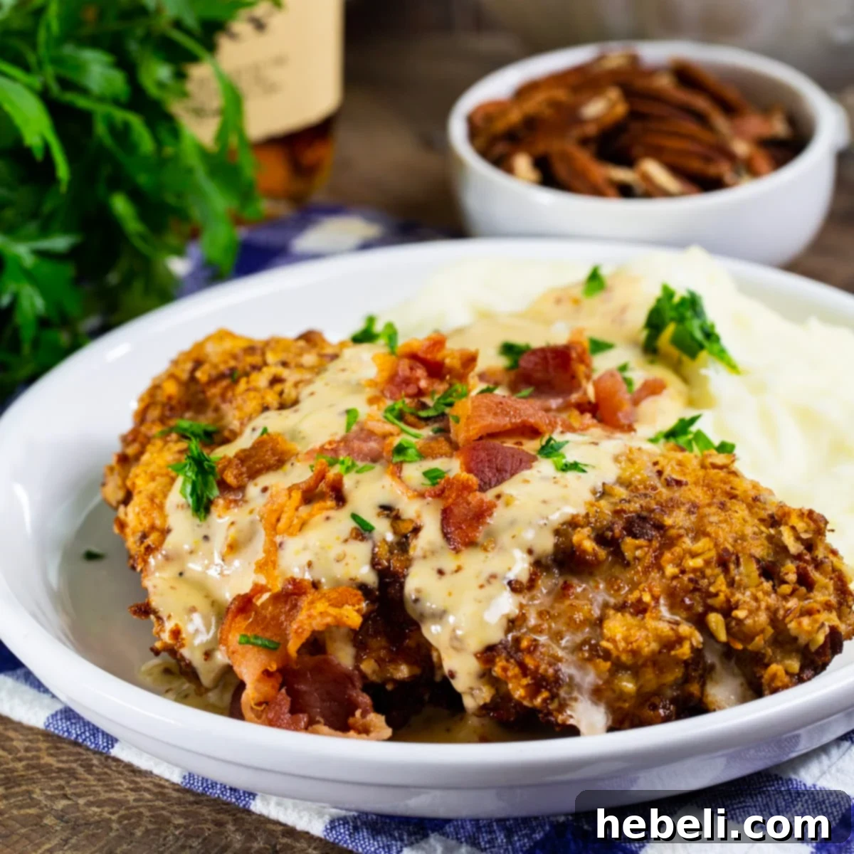 Pecan Chicken in Bourbon Maple Cream Gravy on a plate with mashed potatoes, garnished with bacon.