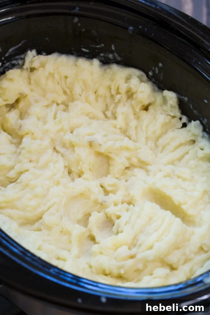 A top-down view of sliced russet potatoes neatly arranged in a slow cooker, covered with cooking liquid, preparing for Crockpot Mashed Potatoes.