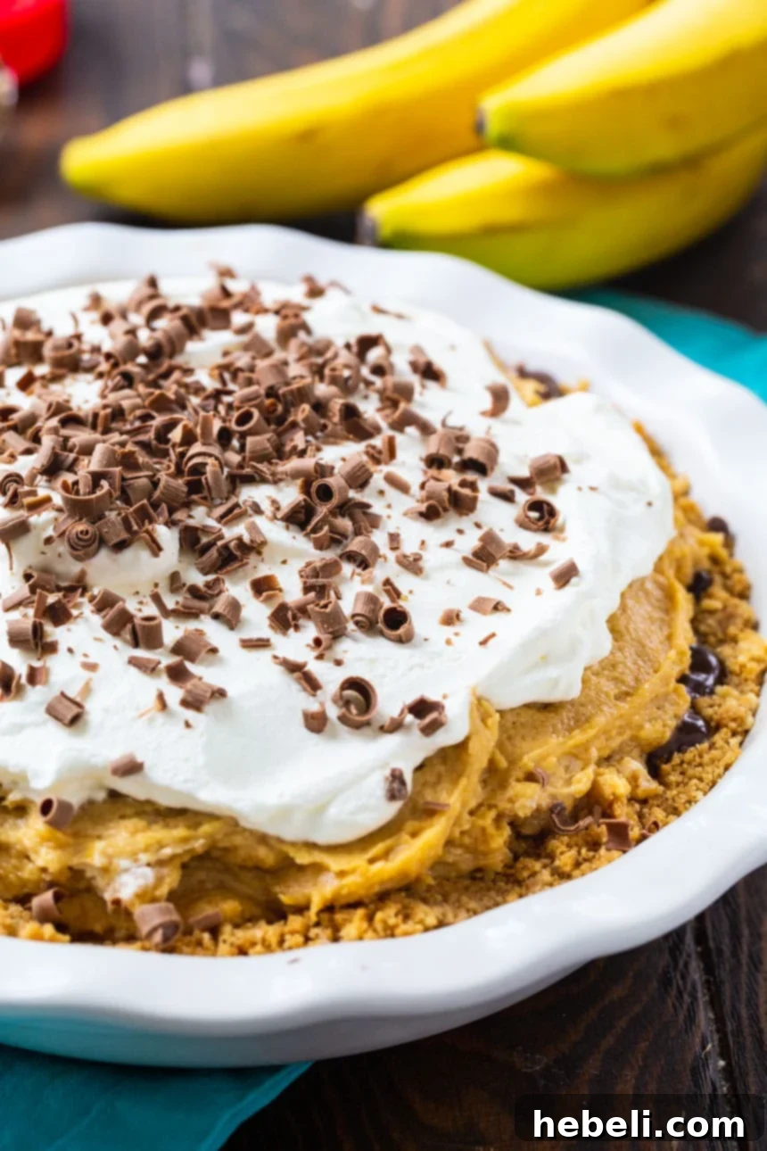 Whole Peanut Butter Banana Pie in a white pie plate with fresh bananas in the background, hinting at the key ingredient.