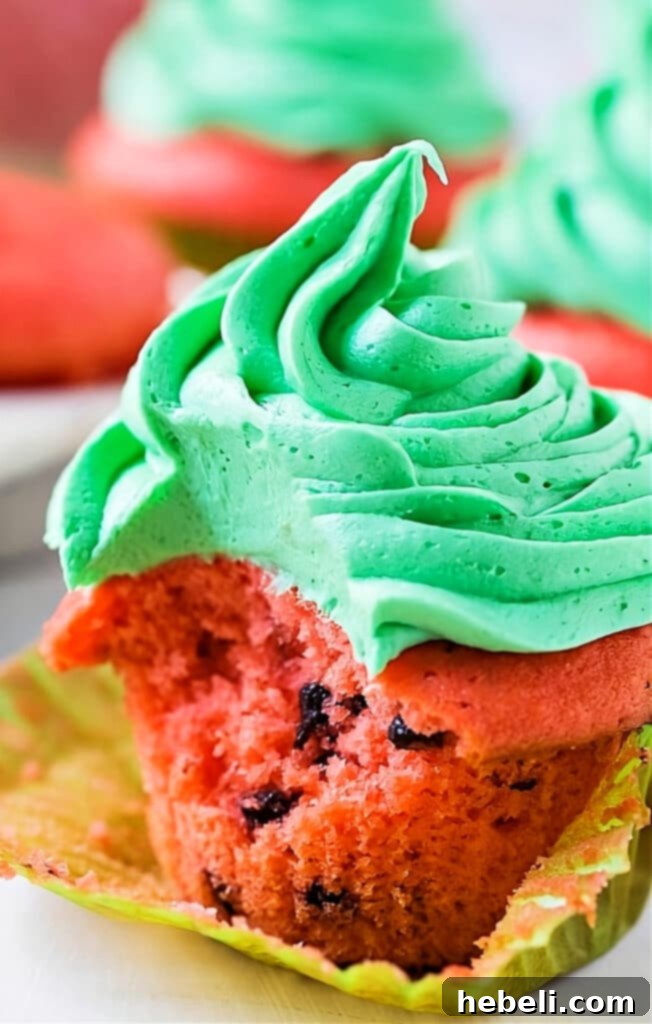 A Watermelon Mojito Cupcake with a portion removed, clearly showing the red cake infused with mini chocolate chips and topped with green mint frosting.