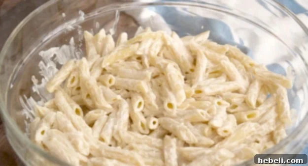 Hearty Chicken Caesar Pasta Salad 3 Pouring half of the creamy Caesar dressing over cooked penne pasta in a large bowl