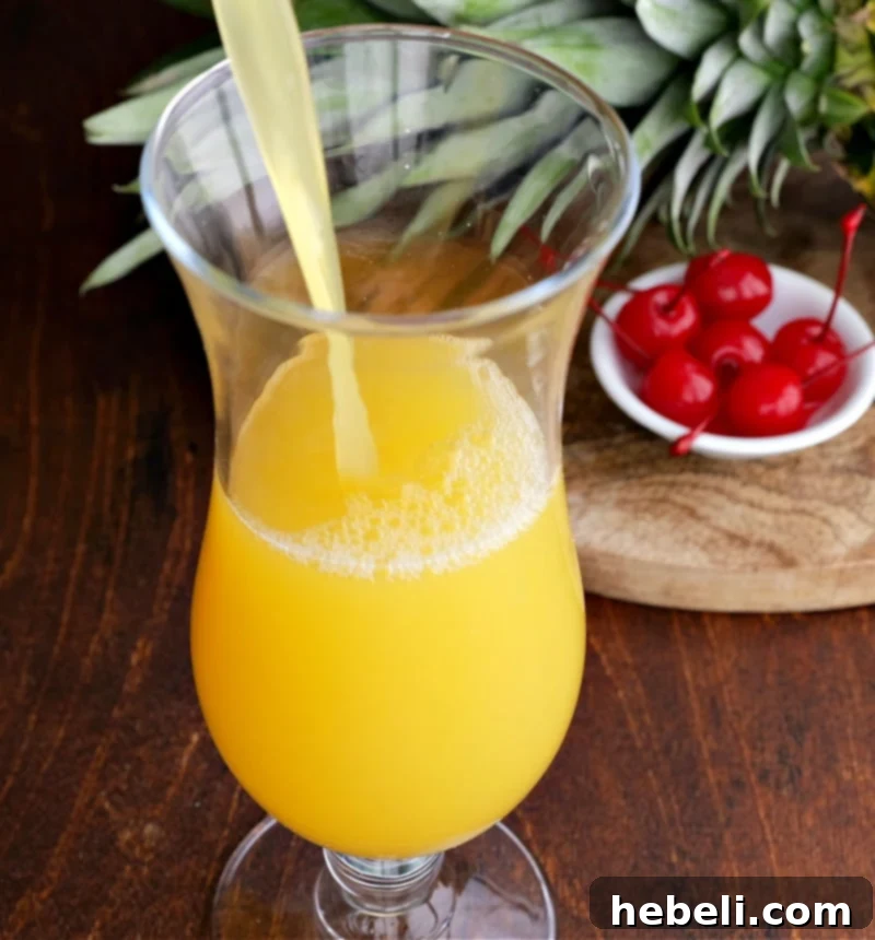 Inverted Aloha 5 The pineapple mixture being poured into a hurricane glass.