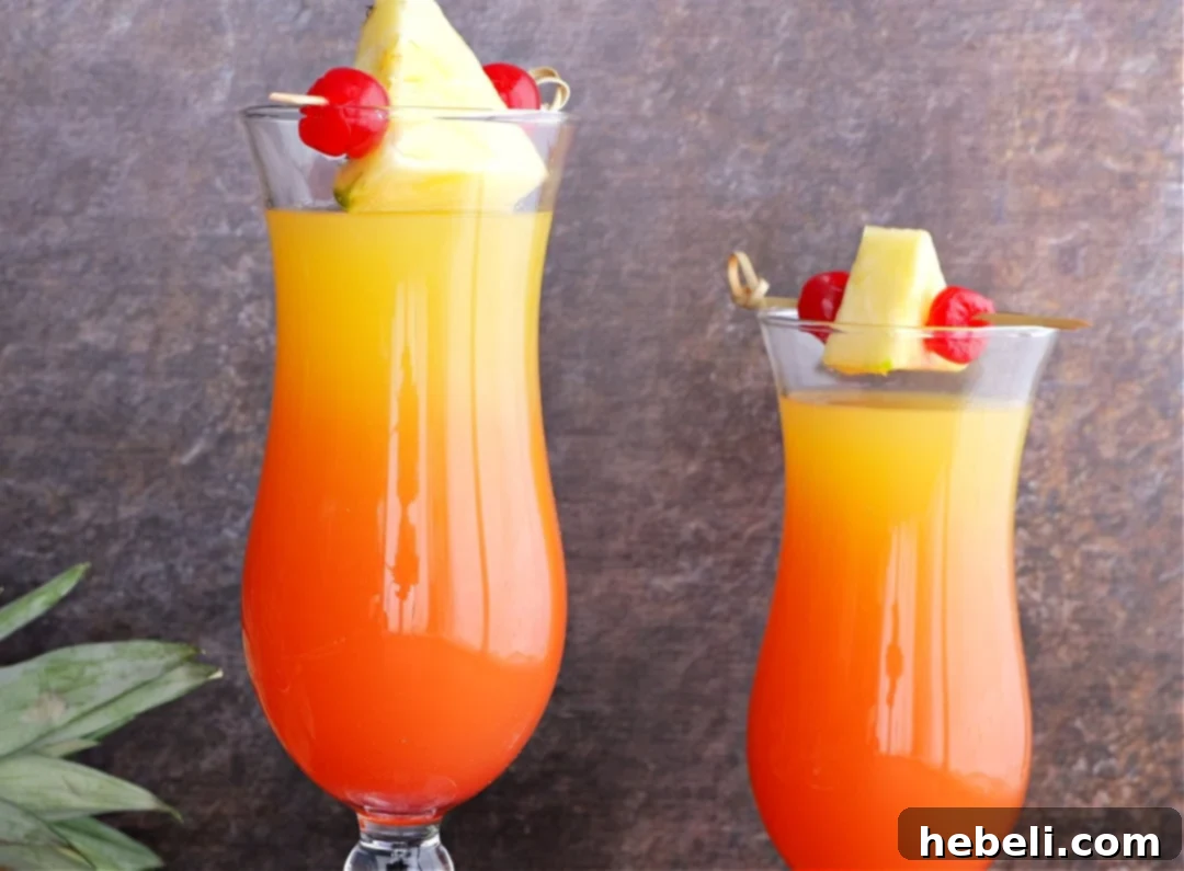 Two finished Pineapple Upside Down Cocktails with cherry and pineapple garnishes.
