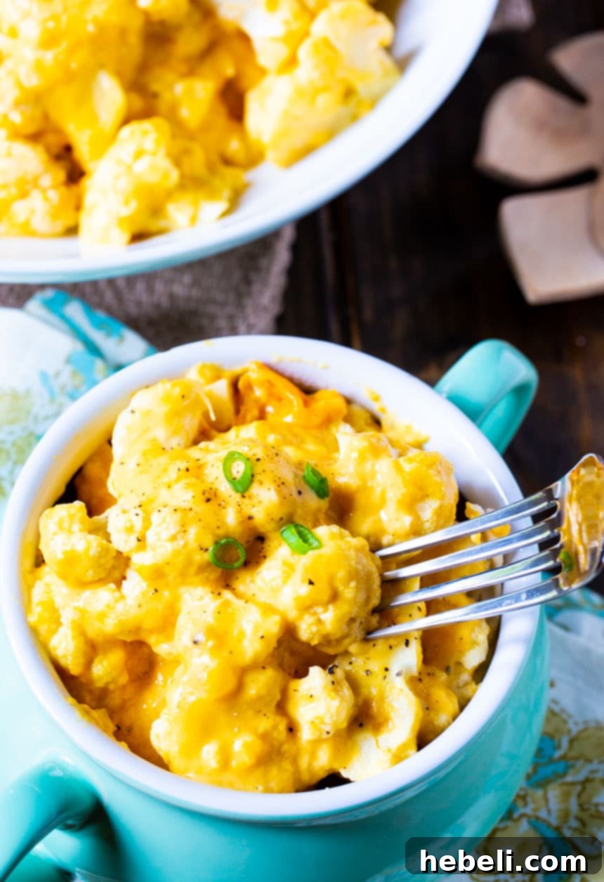 Creamy Slow Cooker Cheesy Cauliflower 3 A fork lifting a piece of perfectly cooked, cheesy cauliflower from a bowl, showcasing its creamy texture.