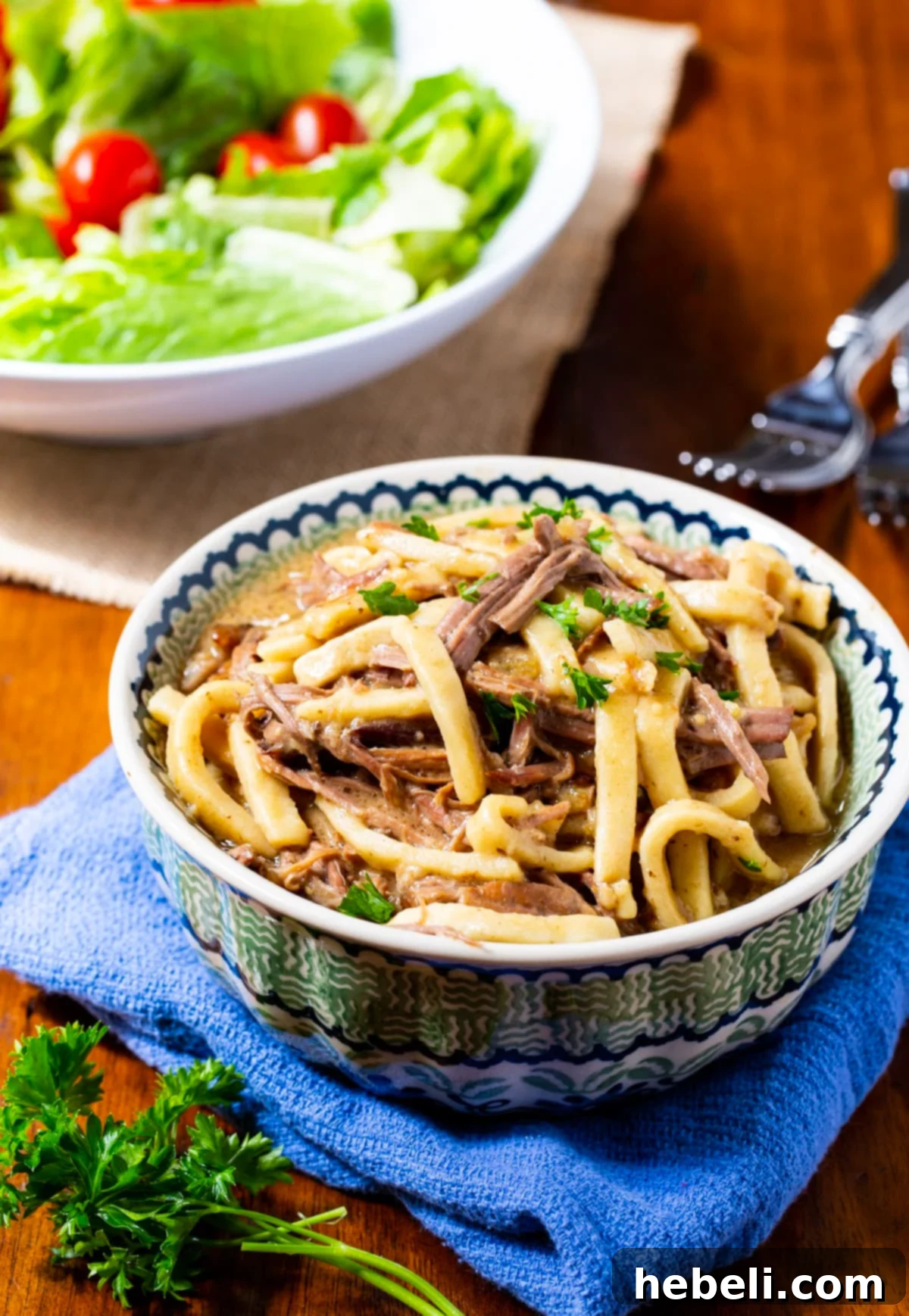 Ultimate Slow-Cooked Beef Noodles 3 A bowl of Crock Pot Beef and Noodles served alongside a fresh green salad, highlighting a balanced and comforting meal option.