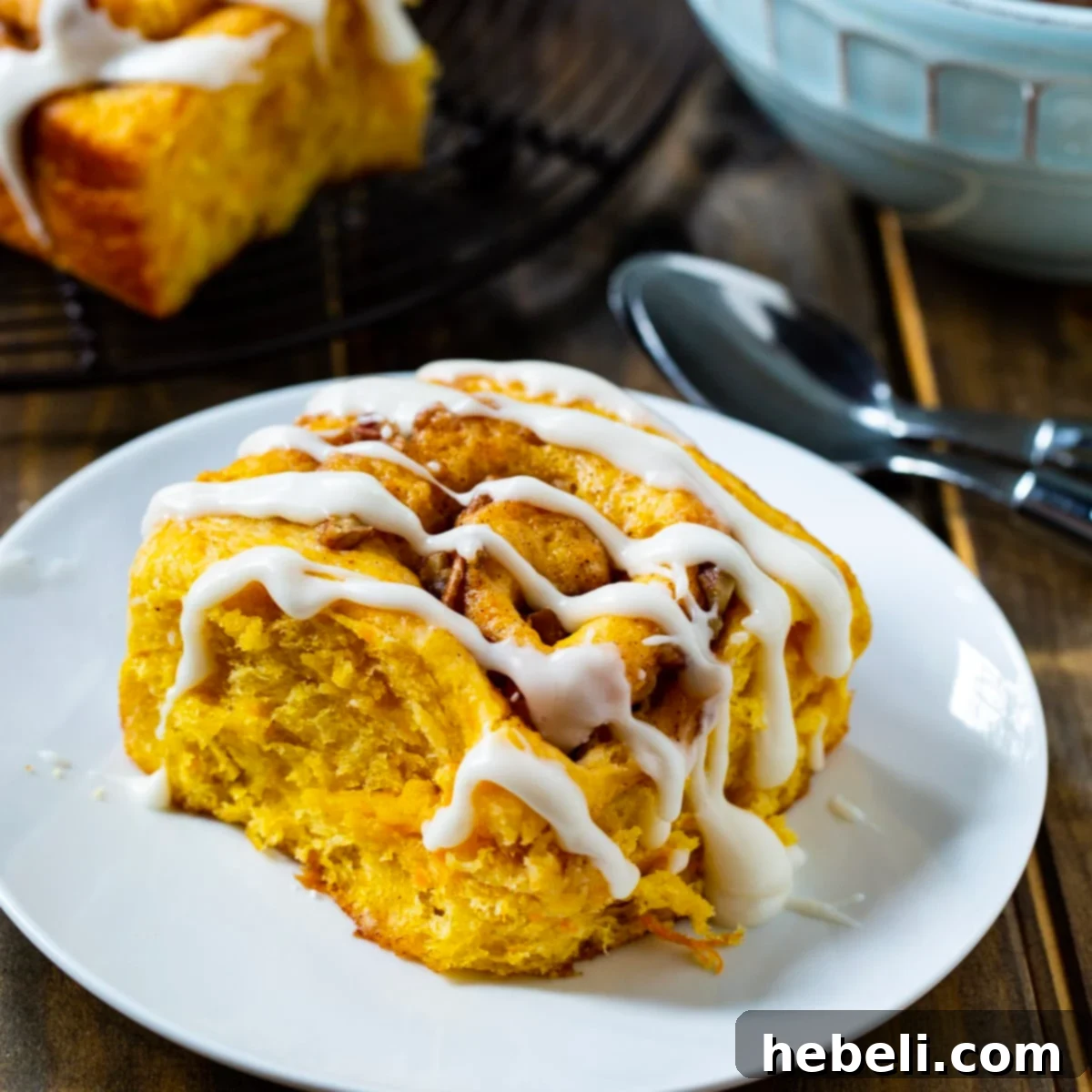 A single, perfectly baked sweet potato cinnamon roll on a white plate, showcasing its golden-brown exterior, swirled filling, and generous drizzle of sweet glaze.