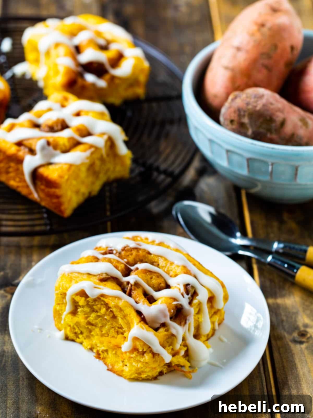 A cluster of freshly baked sweet potato cinnamon rolls on a wire rack next to a bowl of cooked sweet potato mash, illustrating the key ingredient.
