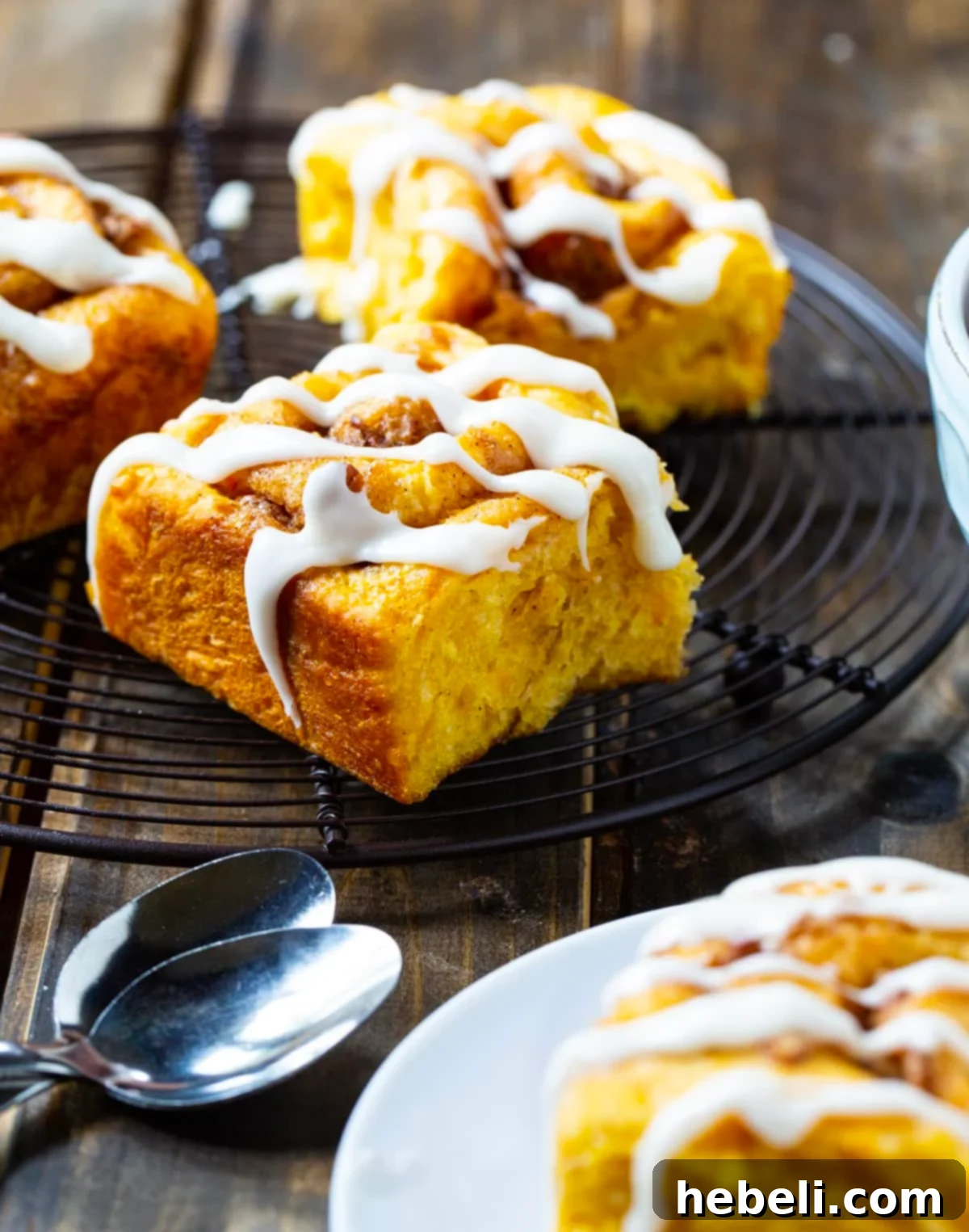 Freshly baked sweet potato cinnamon rolls, glistening with glaze, cooling on a wire rack.