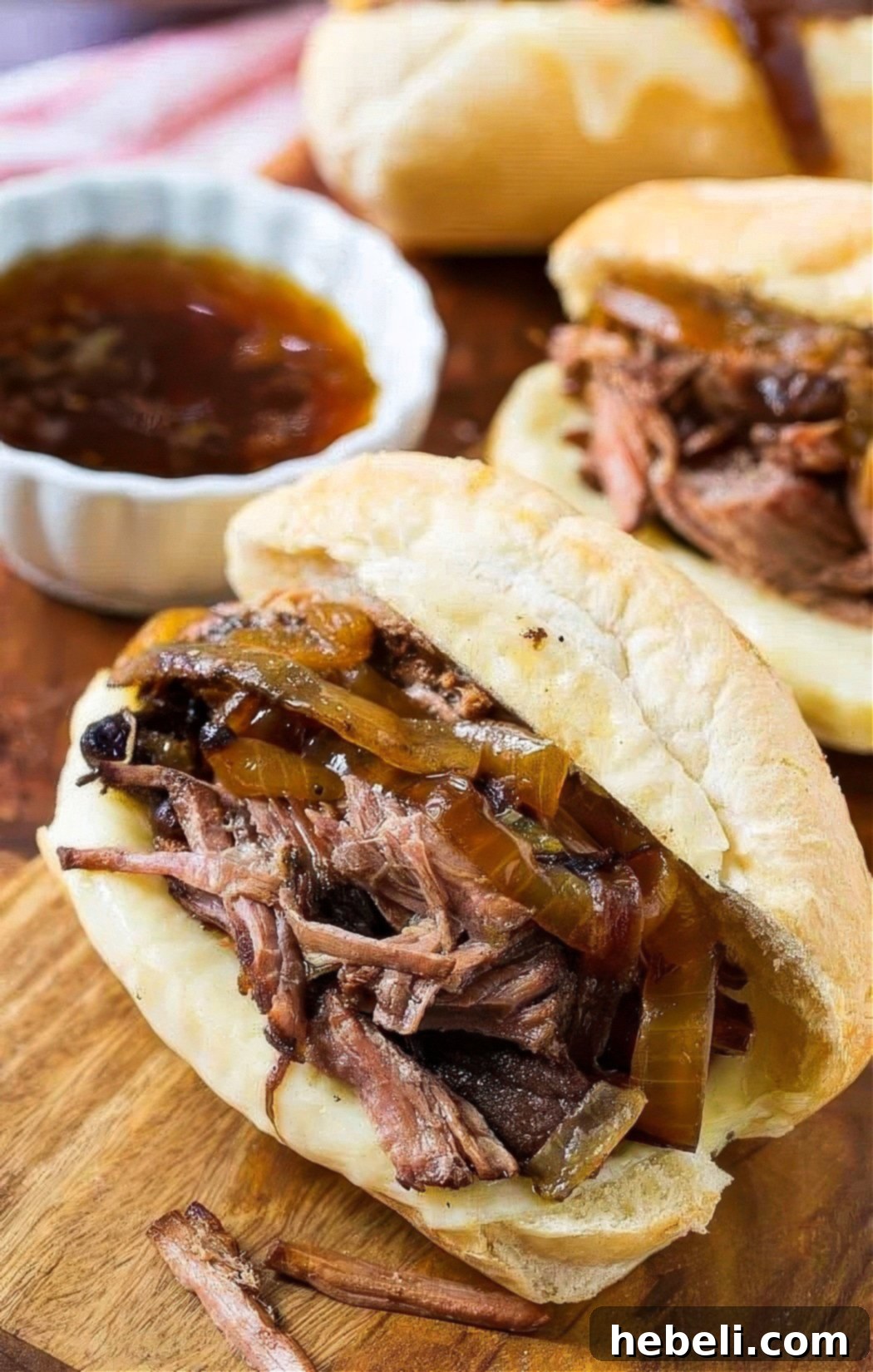 A perfectly assembled French Dip Sandwich with generous beef and melted provolone, ready to be dipped into a small bowl of au jus.
