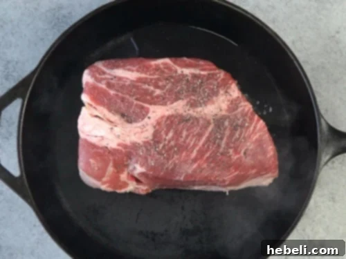 Searing a boneless chuck roast in a skillet until browned on both sides.
