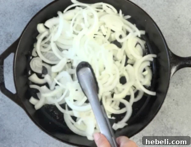 Sliced onions cooking in beef juices in a skillet until softened.