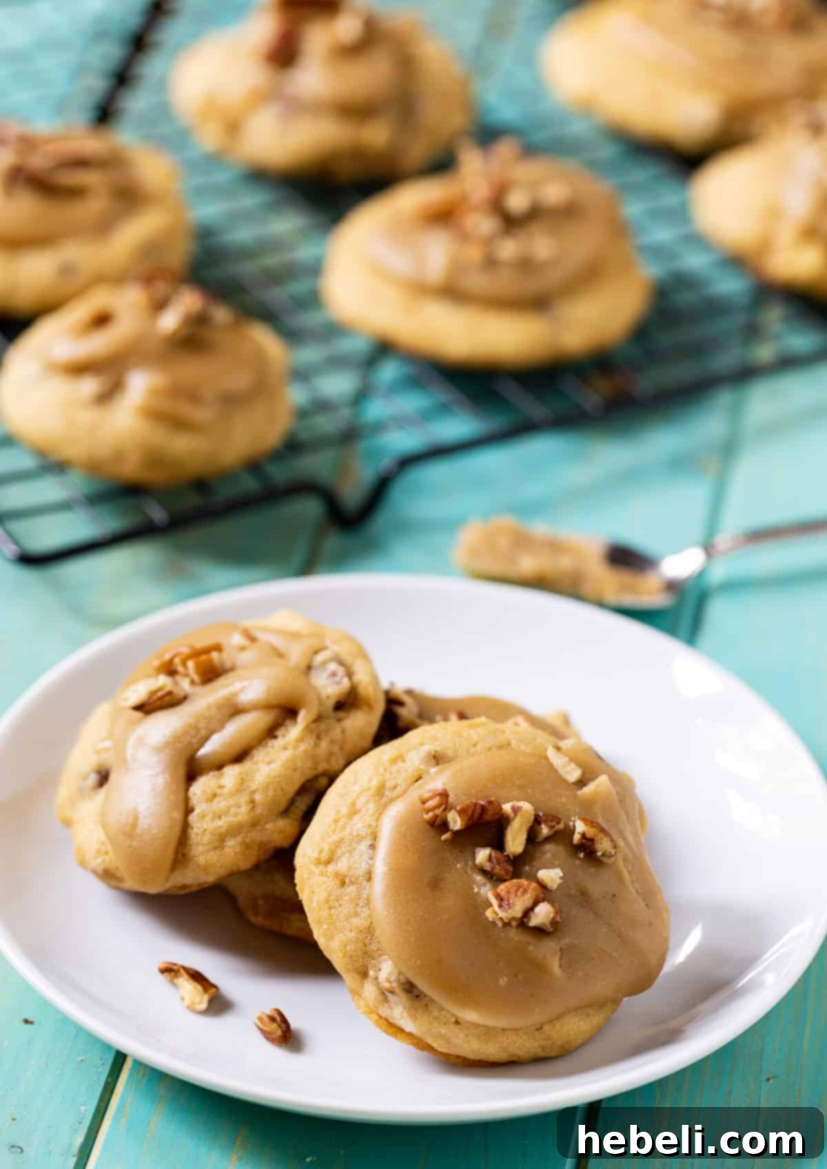 A plate of Caramel Frosted Brown Sugar Cookies next to a cooling rack with more cookies.