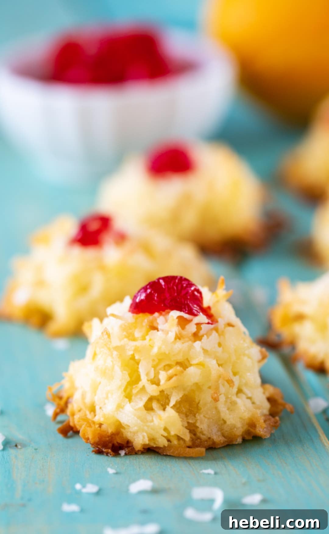 Close-up of Ambrosia Macaroons on a vibrant blue surface, showing their texture and cherry topping.