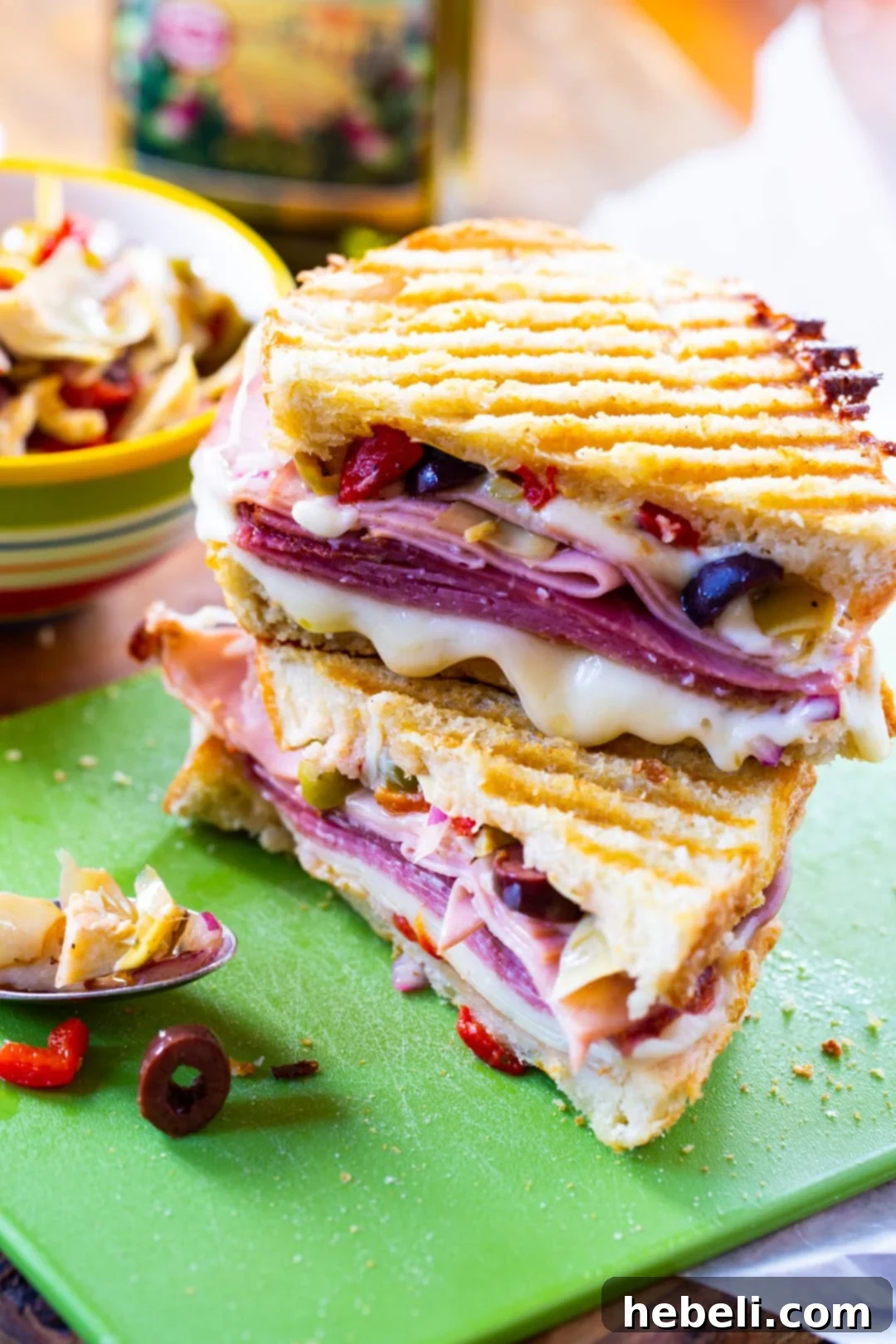 Panini on cutting board with bowl of olive salad, ready for serving.