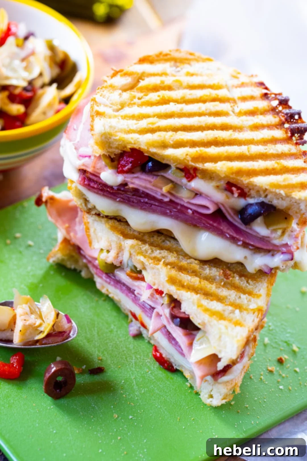 Muffaletta Panini sliced in half, showing the rich layers of meat and cheese.