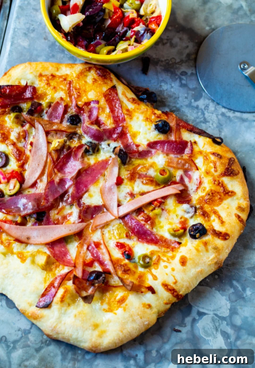 New Orleans Muffaletta Pizza 3 A whole Muffaletta Pizza alongside a bowl of freshly prepared olive salad, highlighting the key ingredients of this unique dish.