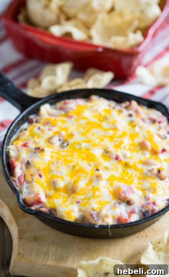 Fiery Black-Eyed Pea Delight 4 A serving of hot, cheesy black-eyed pea dip, garnished and ready to be enjoyed with chips, perfect for New Year's or Superbowl parties.