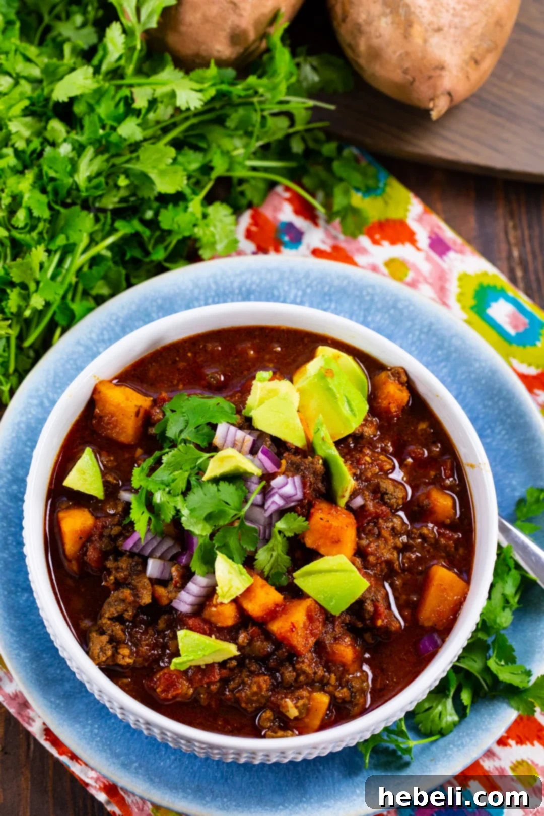 A bowl of Beef and Sweet Potato Chili, beautifully garnished with fresh avocado, red onion, and cilantro.