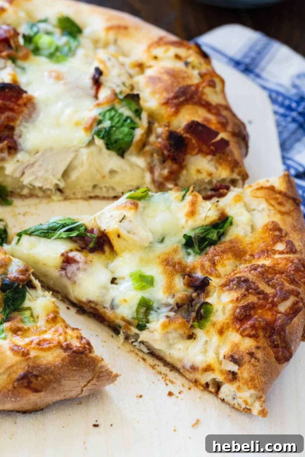 A perfectly cut slice of homemade Chicken Alfredo Pizza, pulled slightly from the main pie, highlighting the melted cheese and fresh toppings.