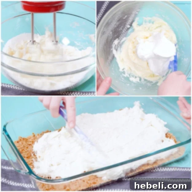 The smooth, white cream cheese layer being carefully spread over the baked and cooled pretzel crust in a glass baking dish.