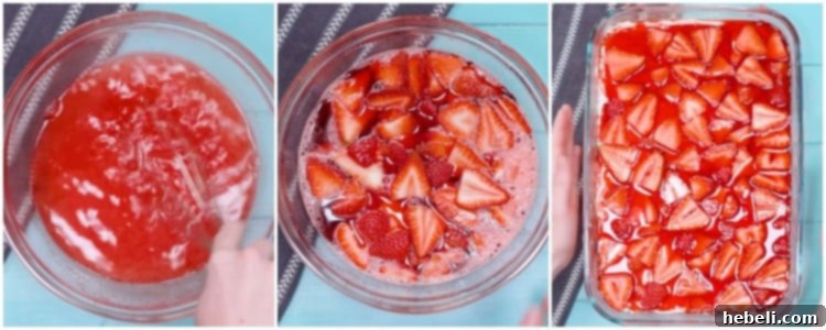 The final layer of bright red strawberry Jell-O with fresh strawberry slices poured over the white cream cheese layer in a baking pan.
