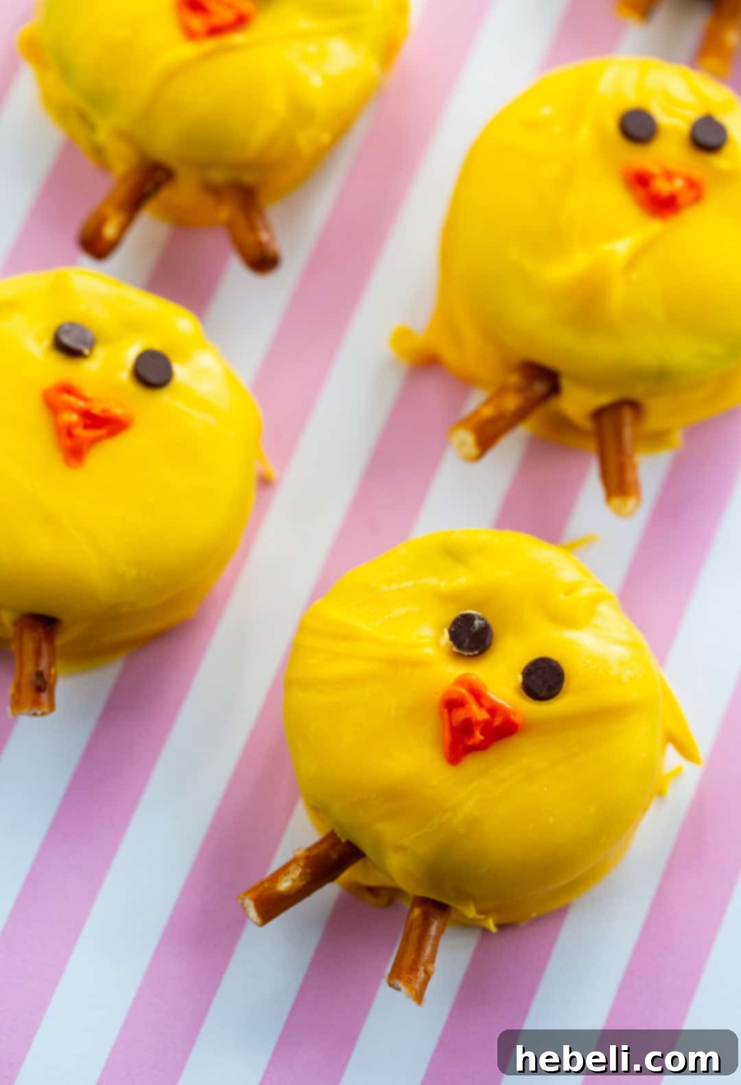 Hoppy Oreo Chicks 3 A close-up of a perfectly crafted Oreo Easter Chick, featuring bright yellow candy coating, mini chocolate chip eyes, and pretzel rod legs, set against a soft pink and white background.