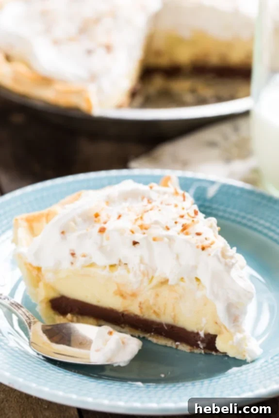 Black Bottom Coconut Cream Pie topped with generous whipped cream and golden toasted coconut flakes.
