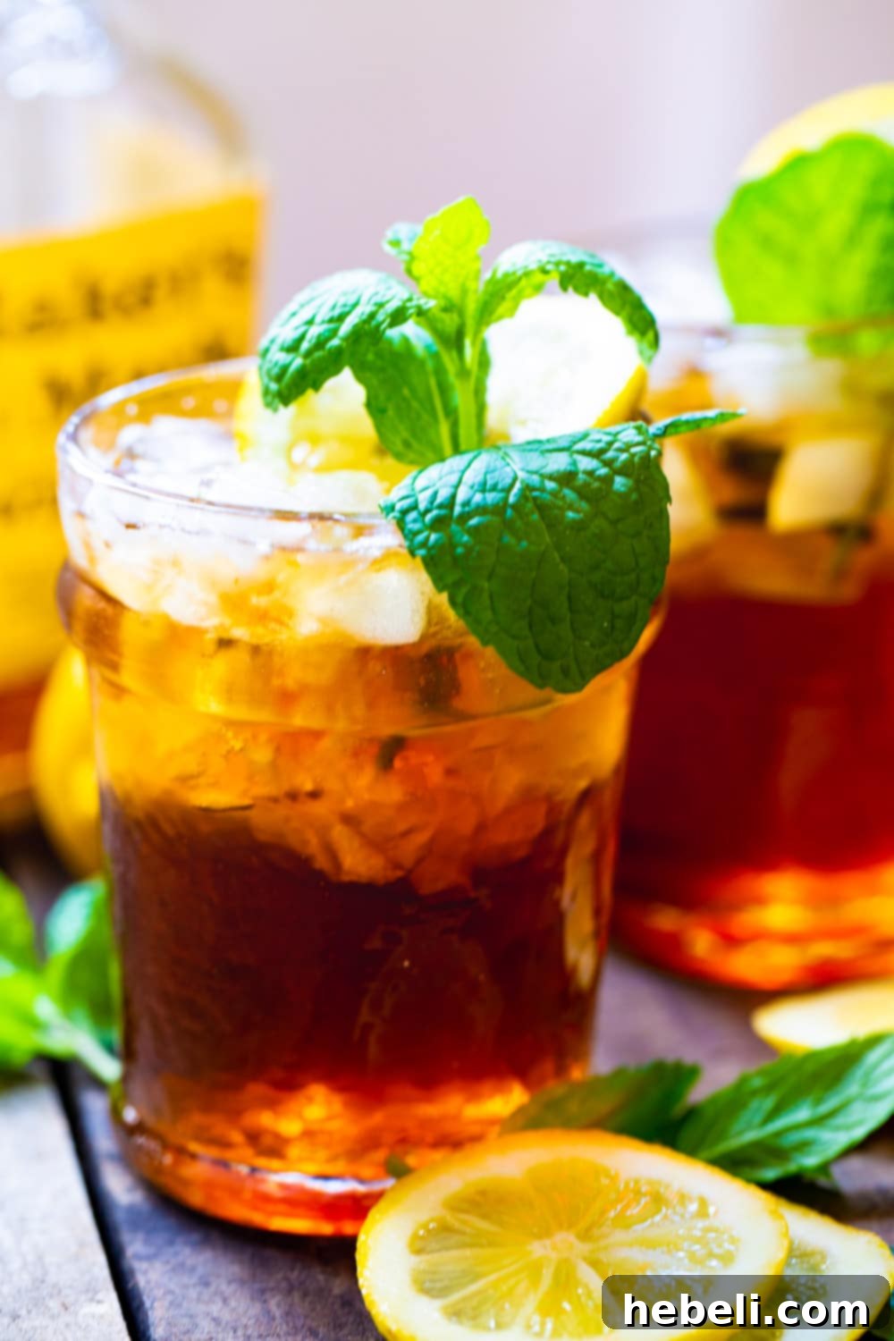Three Sweet Tea Mint Juleps with a bottle of bourbon, showcasing the key ingredients for this delightful drink.
