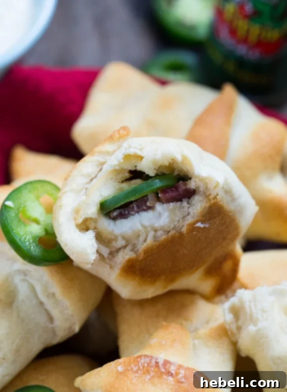 Cheesy Jalapeno Popper Crescent Rolls 5 Close-up of baked Jalapeno Popper Crescent Rolls filled with cream cheese, crispy bacon, and spicy jalapenos, served with a zesty dipping sauce on the side.