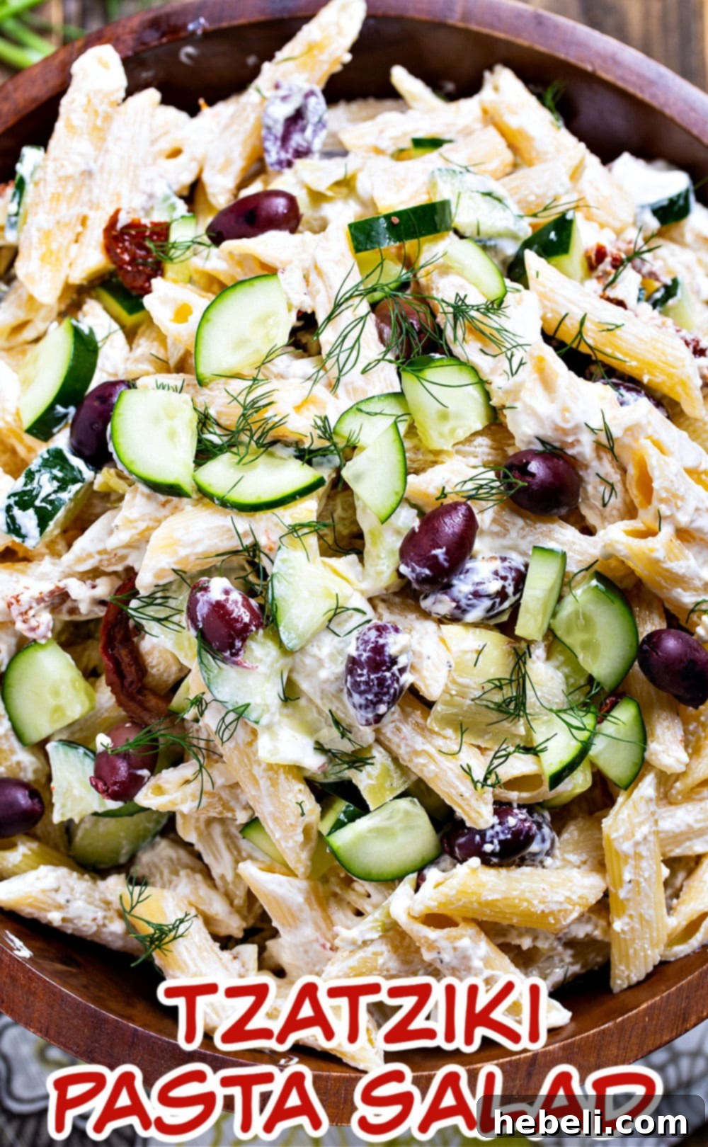 Large wooden bowl of Tzatziki Pasta Salad, garnished with fresh dill and feta cheese.