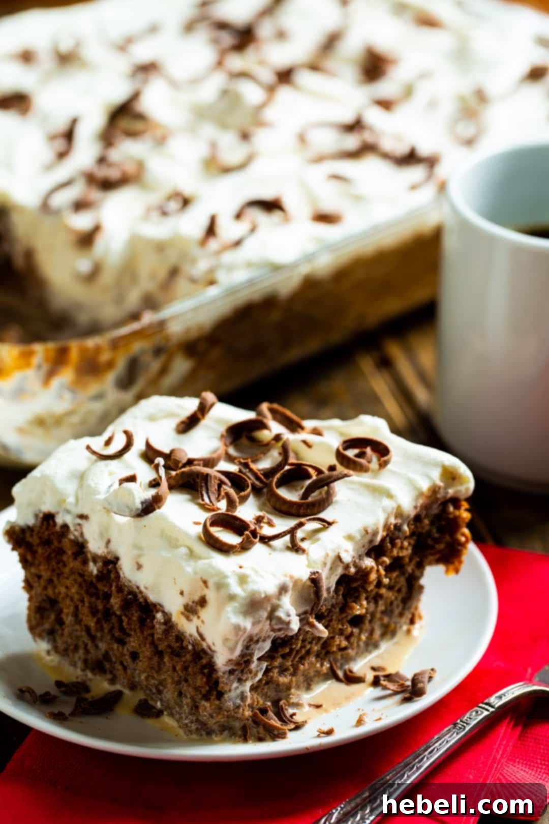 A close-up shot of a slice of Coffee Tres Leches Cake on a plate, with the rest of the cake blurred in the background, highlighting its moist texture.