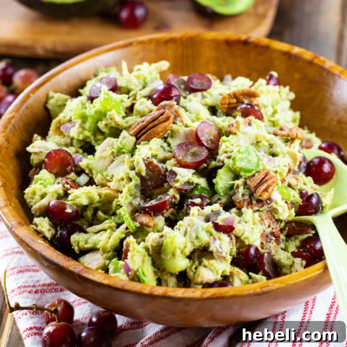 Sonoma Sunshine Chicken & Avocado Salad 2 A beautifully presented bowl of creamy Avocado Sonoma Chicken Salad, garnished with grapes and pecans, in a rustic wooden bowl.