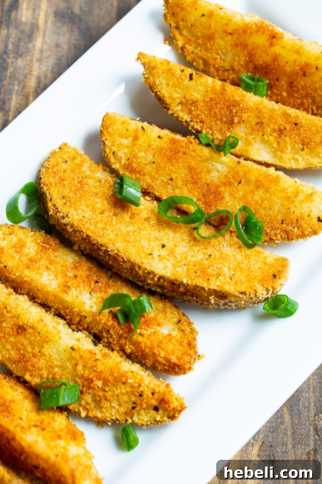 Parmesan Crusted Ranch Potato Wedges arranged on a serving plate, garnished with fresh green onion slices.