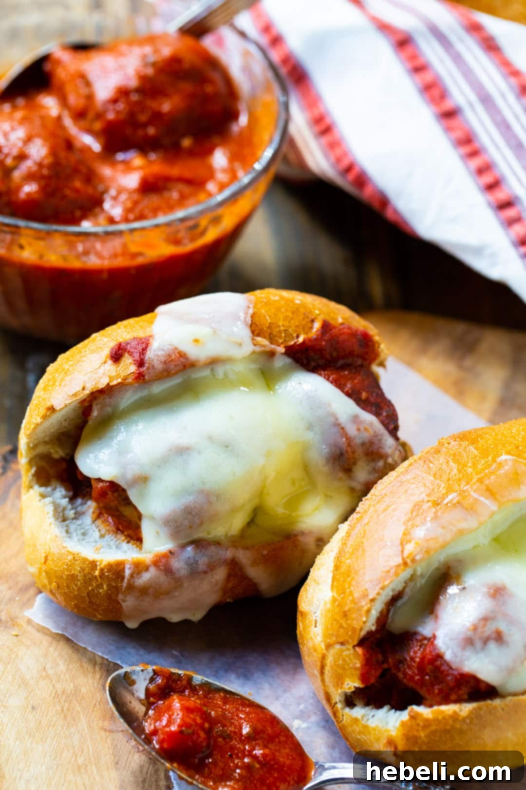 Two perfectly assembled Meatball Subs on a rustic wood cutting board.