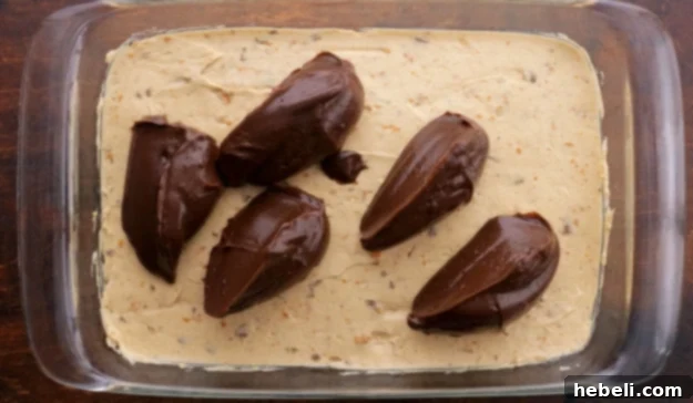 Pouring the prepared chocolate pudding mixture over the peanut butter layer in the baking dish, creating another distinct and appealing layer.