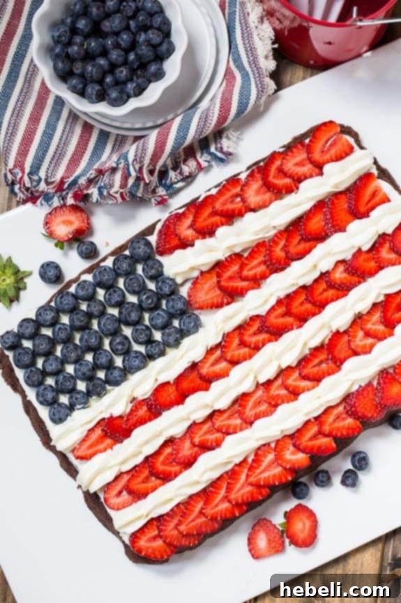 A slice of Flag Brownies showing layers of chocolate, white frosting, strawberries, and blueberries.