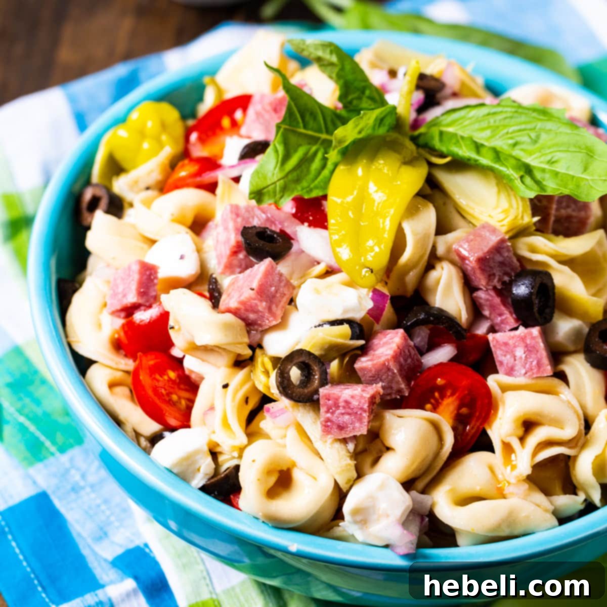Tortellini Antipasto Pasta Salad in a blue bowl, garnished with fresh basil.