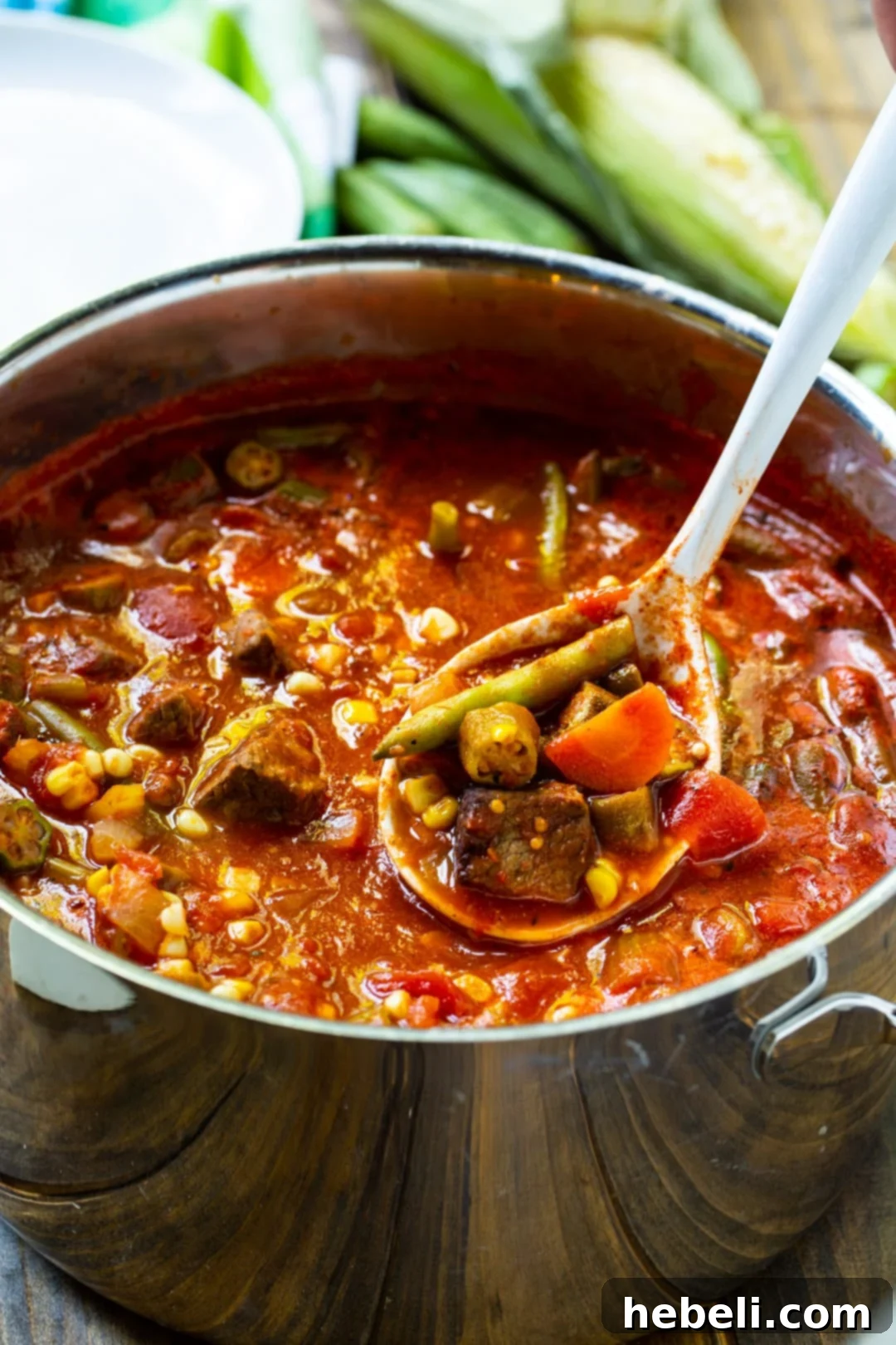 A spoon scooping Vegetable Beef Soup out of a large pot, showing tender beef and vegetables.