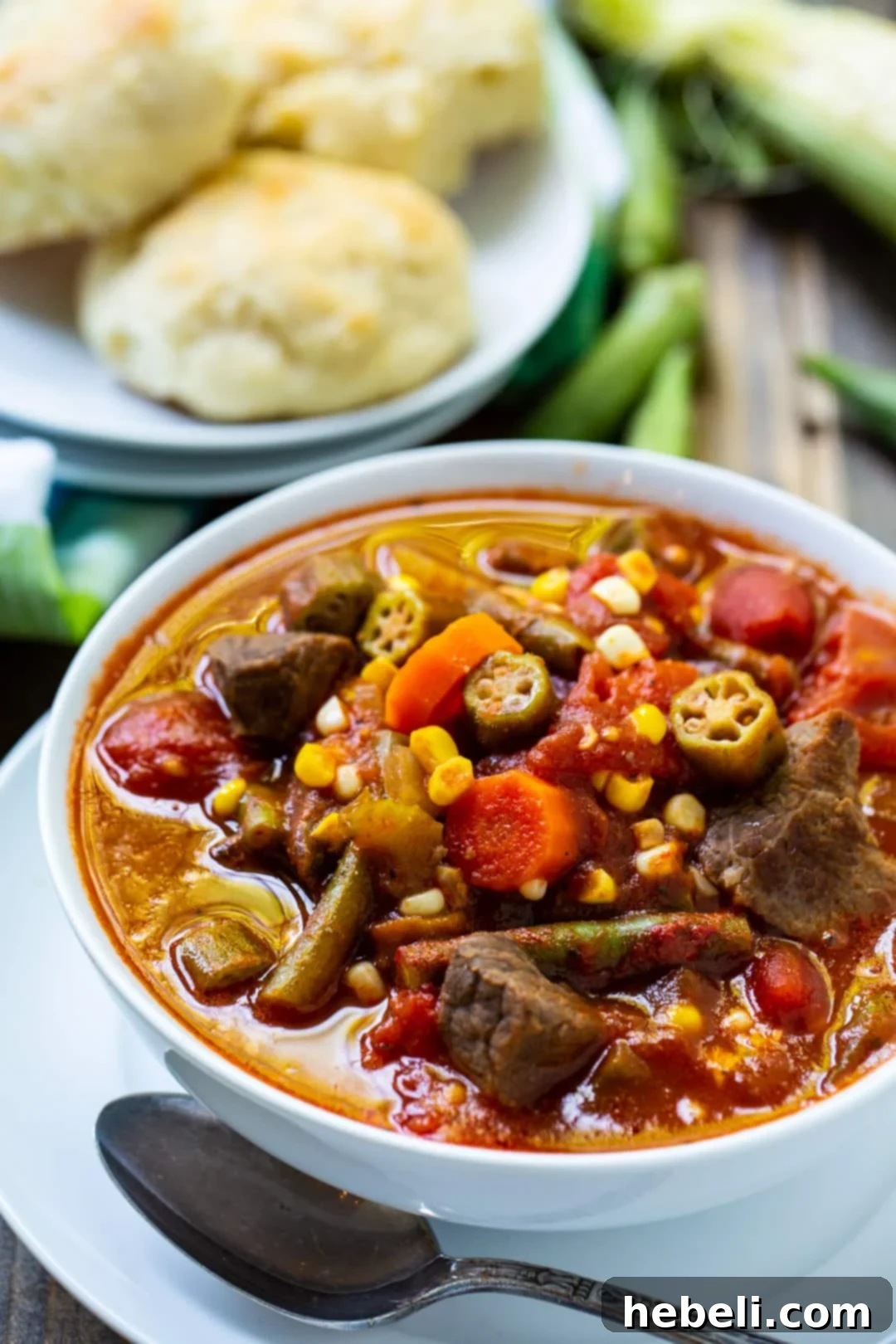 A bowl of Vegetable Beef Soup next to a plate of dinner rolls.