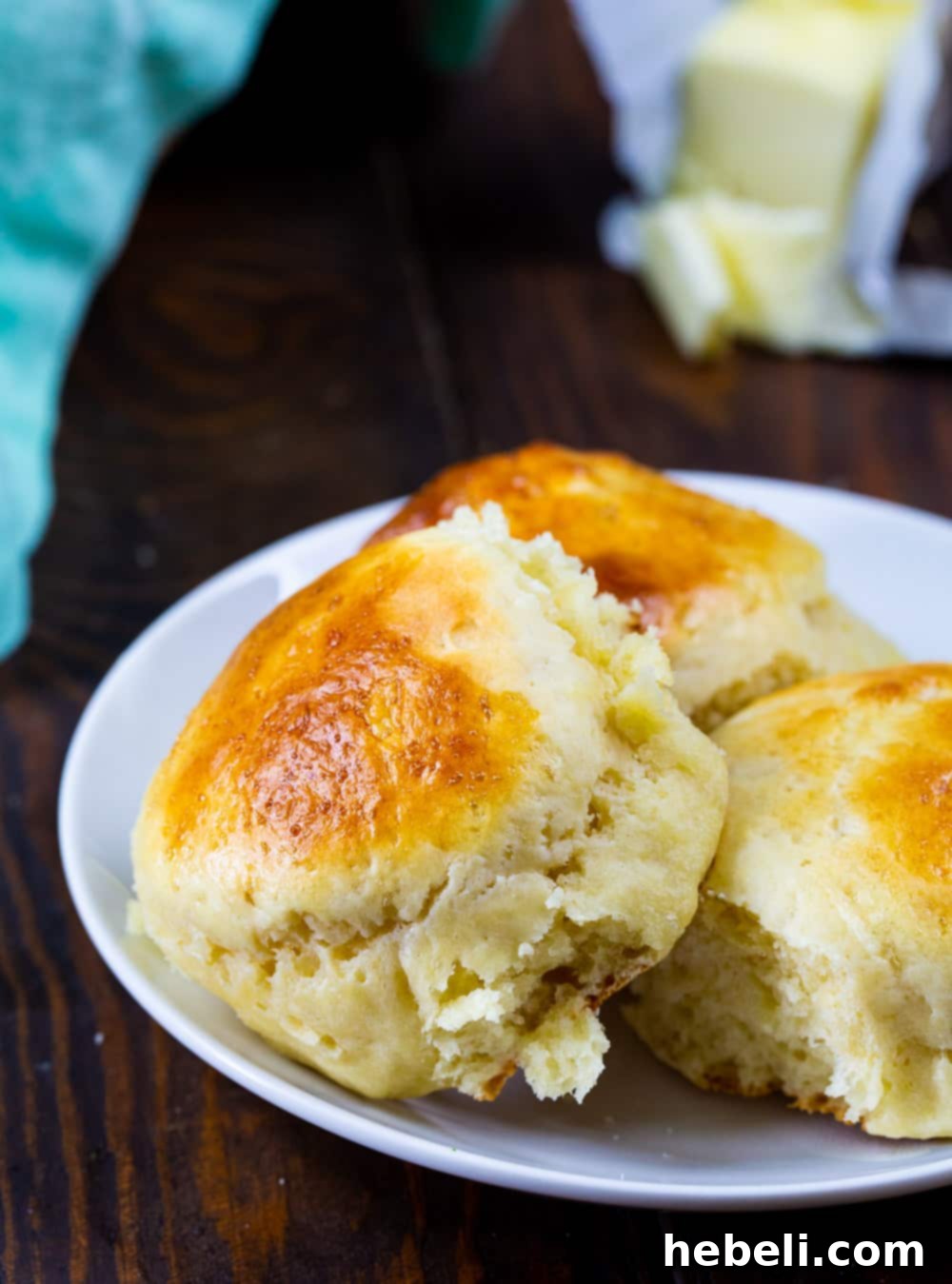 Pillowy Overnight Sour Cream Rolls 4 A close-up of three freshly baked, soft Overnight Sour Cream Rolls on a white plate, highlighting their delicate texture.
