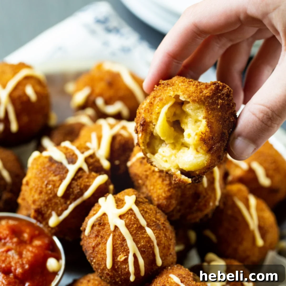 Hand picking up a golden-brown Fried Mac and Cheese ball, showcasing its crispy exterior.