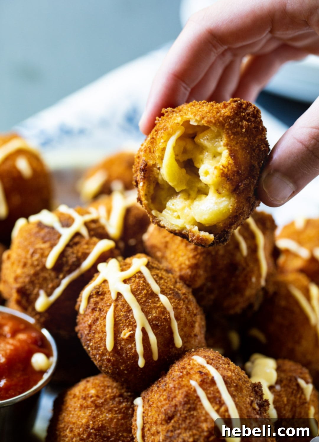 A hand holding a single, perfectly golden fried mac and cheese ball, highlighting its appealing texture.