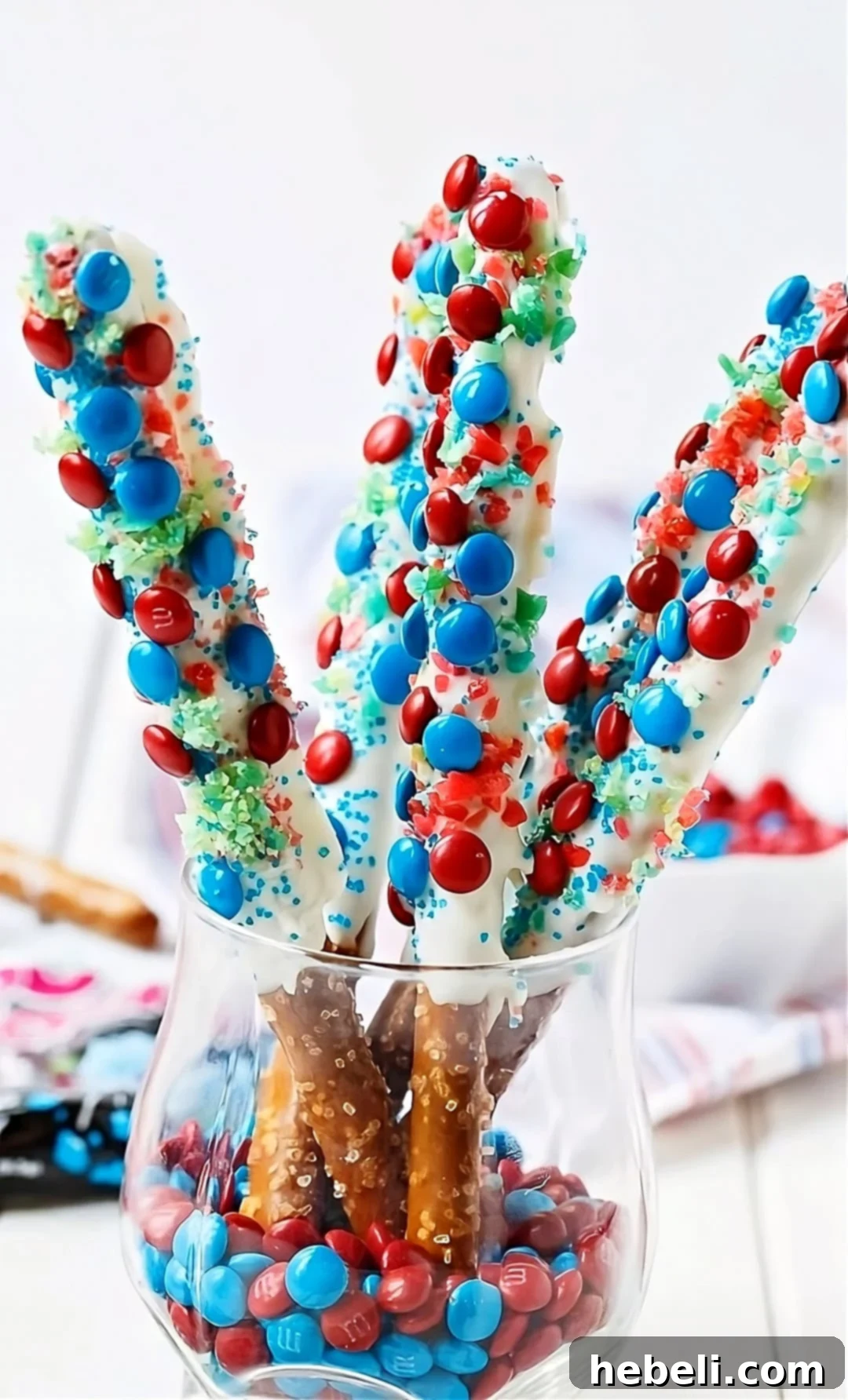 Flavor Burst Pretzel Rods 3 Close-up of Firecracker Pretzel Rods coated in white chocolate and festively adorned with red and blue sprinkles and mini M&Ms.