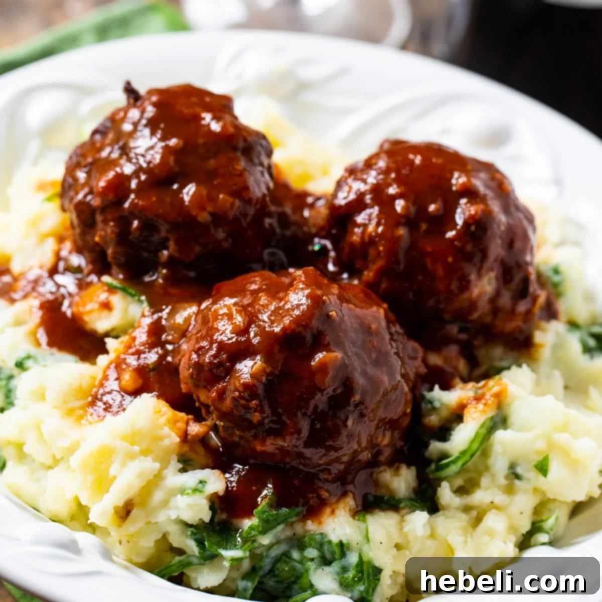 Three perfectly braised meatballs resting on a bed of vibrant green spinach mashed potatoes, ready to be enjoyed.