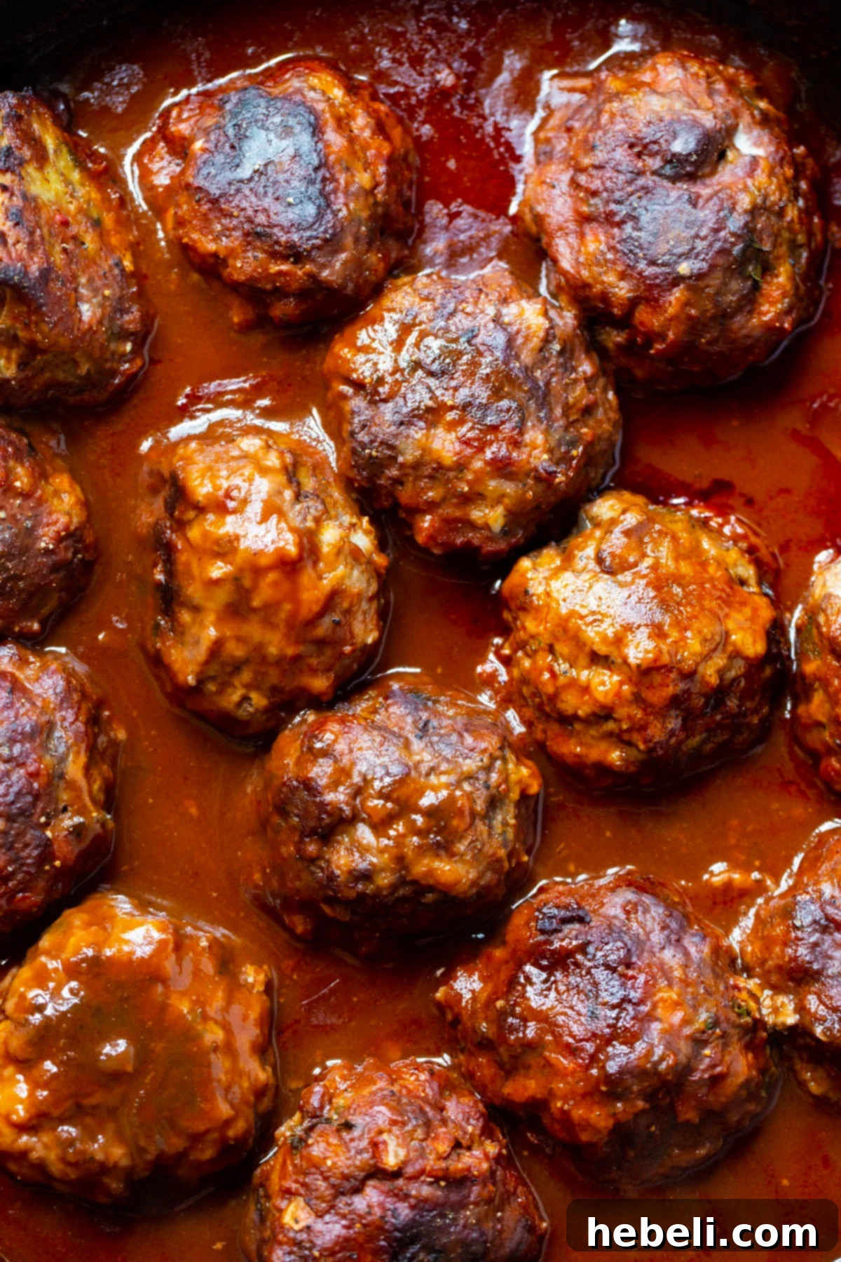 Braised Meatballs in a rich red wine gravy simmering in a cast iron skillet, showcasing the deep color and texture of the sauce.