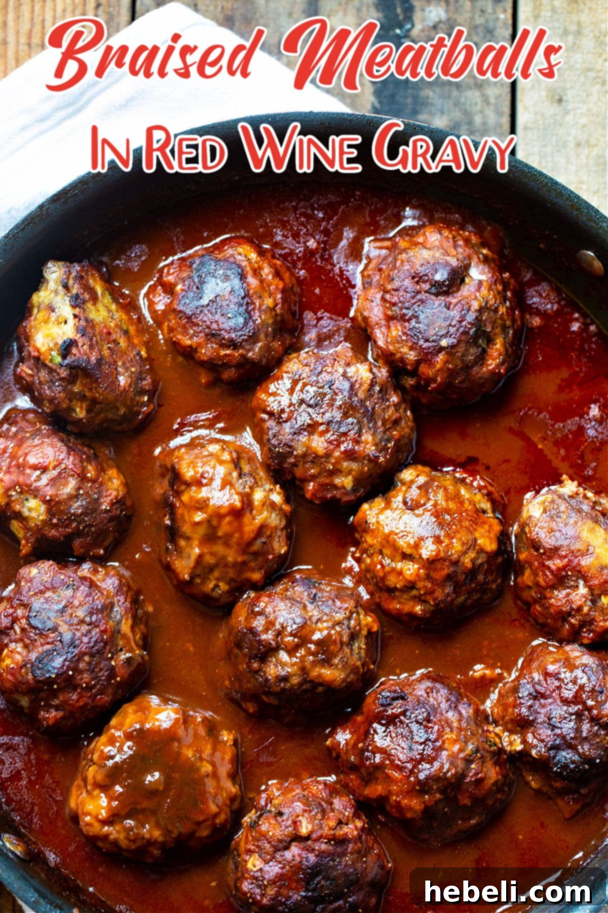 A close-up shot of Braised Meatballs in Red Wine Gravy in a rustic skillet, highlighting the succulent texture of the meatballs and the glossy, thick gravy.