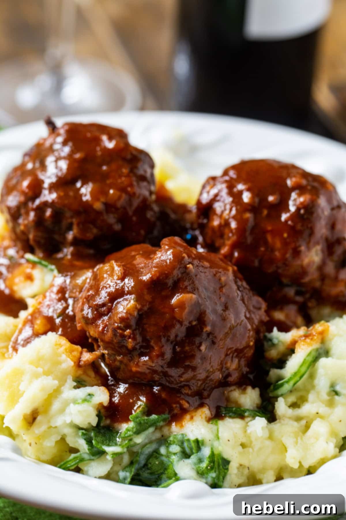 A portion of three delicious braised meatballs generously coated in red wine gravy, served atop creamy mashed potatoes, ready to be enjoyed.