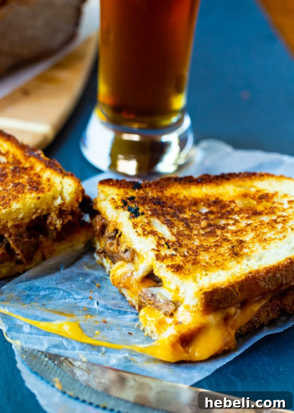 A crispy Brisket Grilled Cheese sandwich, cut in half, next to a glass of refreshing beer.