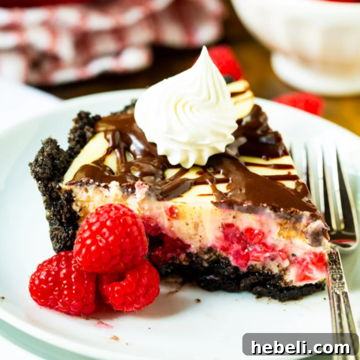 A perfectly sliced Raspberry Cream Cheese Pie on a white plate, garnished with fresh raspberries and a drizzle of chocolate.
